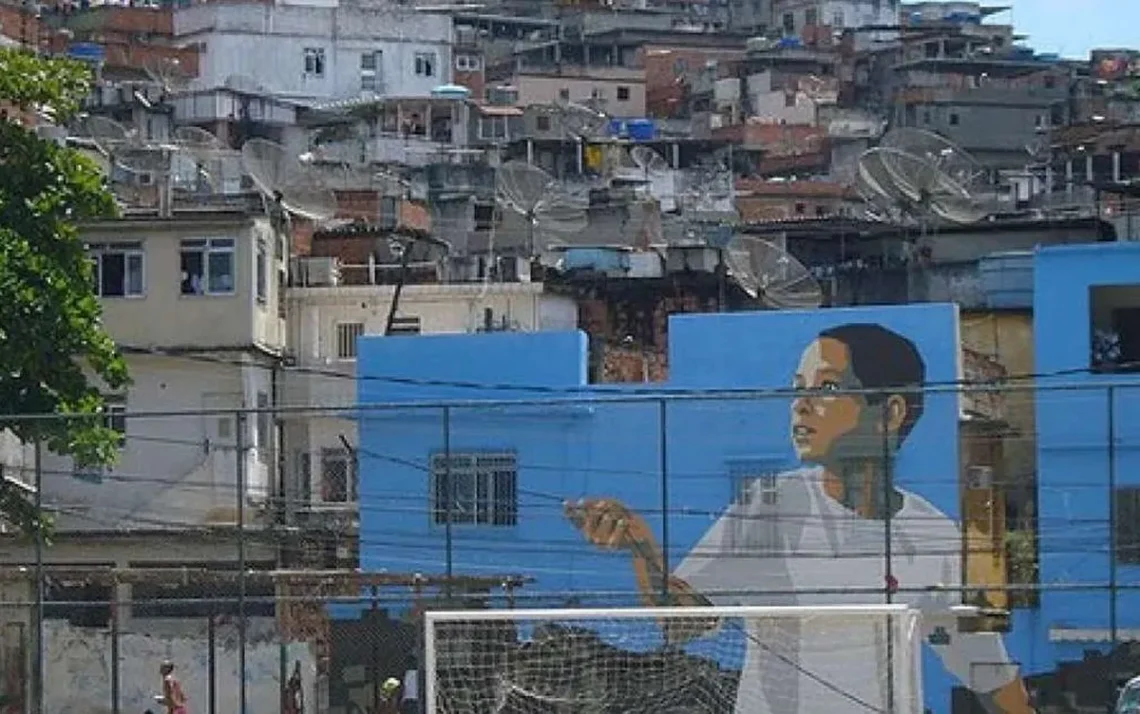 O futebol na Vila Cruzeiro sempre foi importante para a comunidade e preparou o terreno para o surgimento de Adriano, o Imperador. Foto: Facebook Vila Cruzeiro No alto, Igreja da Penha. Morro abrigava quilombo no século 19. Décadas depois, surgem favelas como a Vila Cruzeiro. Foto: Rio Antigo Estátua dos mestres Touro e Dentinho no Largo da Penha, instalada em 2021 em homenagem aos capoeiristas. Foto: Selma Souza/Voz das Comunidades Adriano Imperador desfila na Camisa Verde e Branco, em São Paulo, no Sambódromo do Anhembi, em 2024. Foto: Paulo Pinto/AB - Todos os direitos: @ Terra